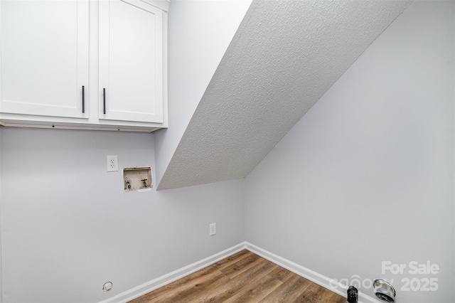 laundry area featuring cabinet space, hookup for a washing machine, a textured ceiling, baseboards, and wood finished floors