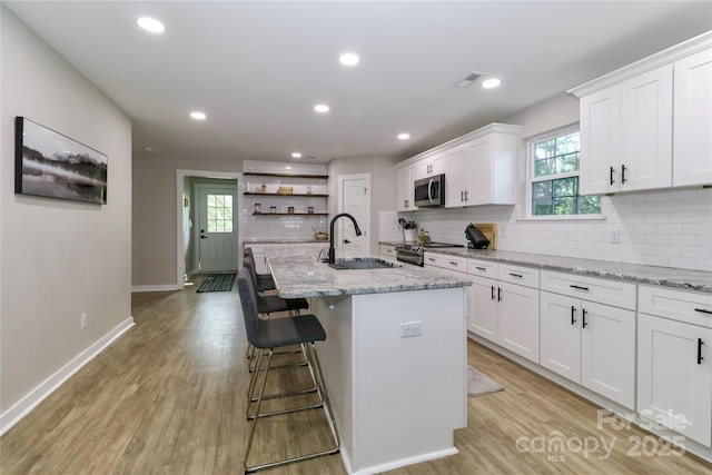 kitchen with a sink, stainless steel appliances, white cabinets, tasteful backsplash, and recessed lighting