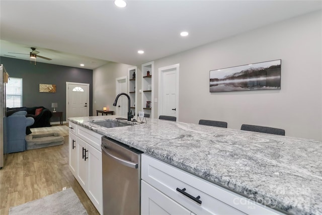 kitchen featuring a sink, stainless steel dishwasher, light wood-type flooring, light stone counters, and white cabinets