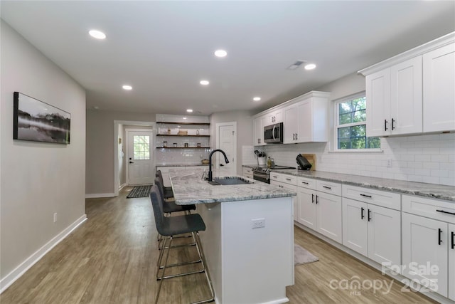 kitchen featuring a sink, stainless steel appliances, open shelves, white cabinetry, and tasteful backsplash