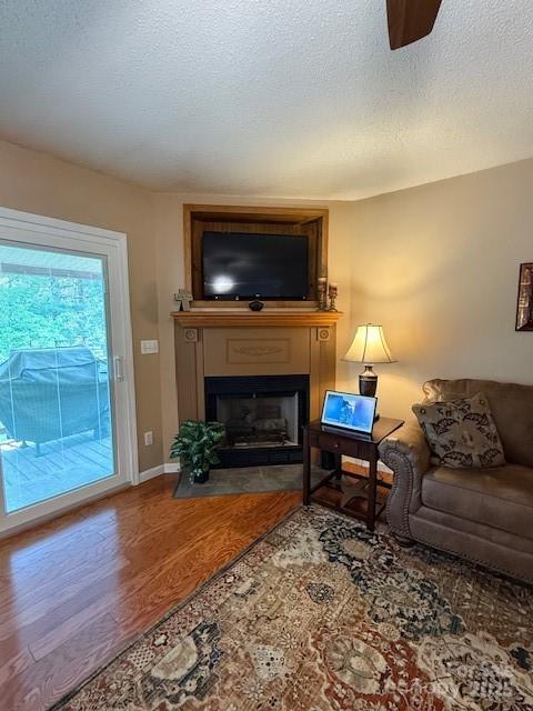 living area featuring wood finished floors, a textured ceiling, a ceiling fan, and a large fireplace