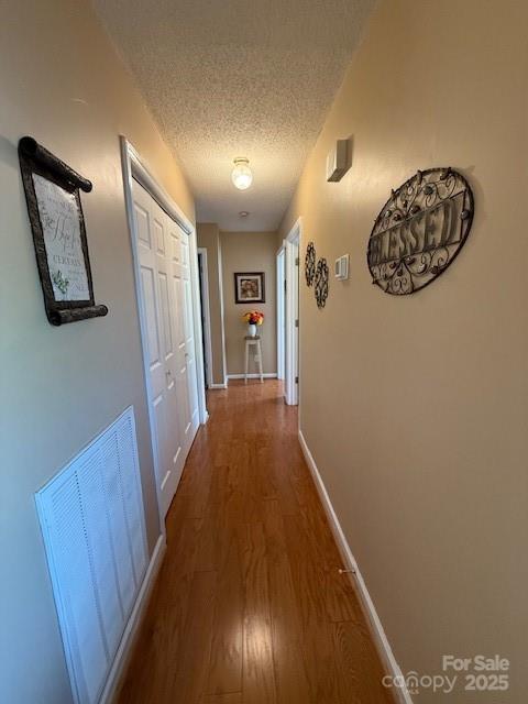 hallway featuring wood finished floors, a textured ceiling, and baseboards