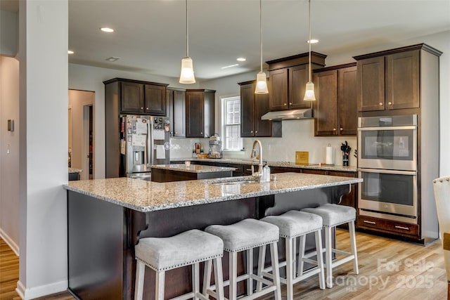 14925 Baldridge Dr, Huntersville, NC 28078 - kitchen with stainless steel appliances, a sink, an island with sink, light wood finished floors, and under cabinet range hood