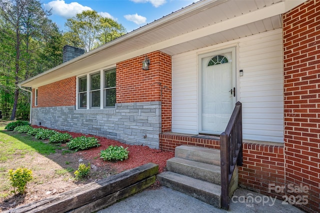 view of exterior entry with a chimney and brick siding
