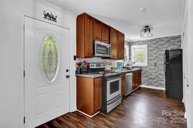 kitchen featuring a sink, appliances with stainless steel finishes, baseboards, ornamental molding, and dark wood-style floors
