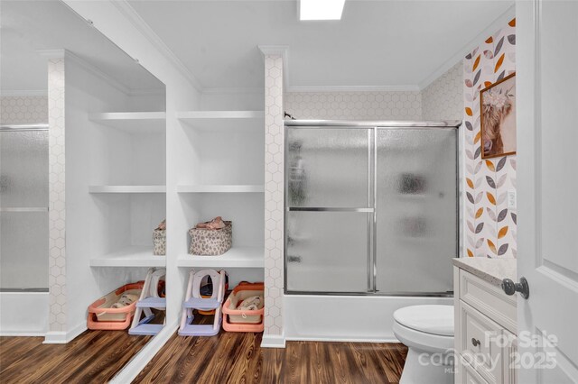 bathroom with shower / bath combination with glass door, wood finished floors, toilet, ornamental molding, and built in shelves