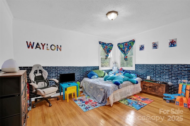 bedroom featuring crown molding, wood finished floors, a textured ceiling, and a wainscoted wall