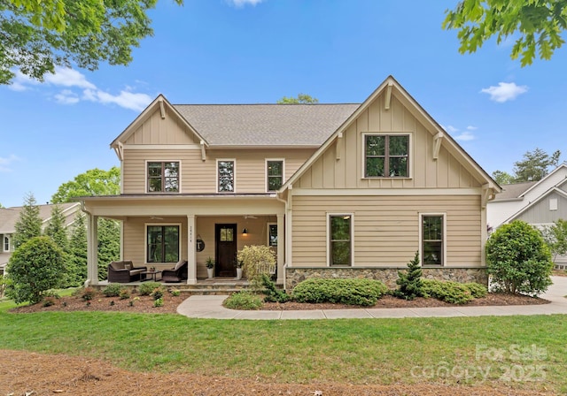 craftsman house with an outdoor living space, a front lawn, stone siding, board and batten siding, and roof with shingles