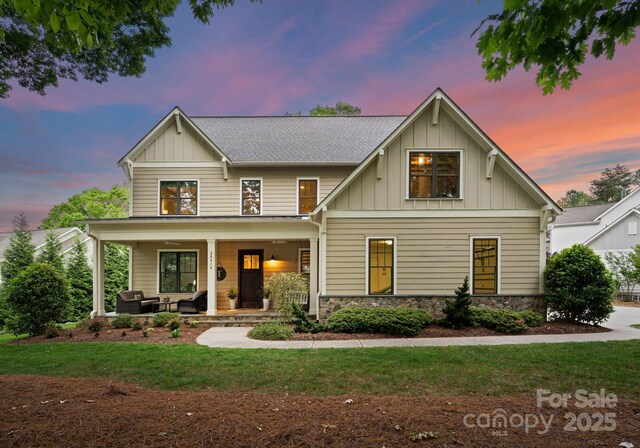view of front of home with a front lawn, stone siding, covered porch, outdoor lounge area, and board and batten siding