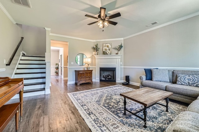 living room featuring a ceiling fan, wood finished floors, visible vents, ornamental molding, and stairway