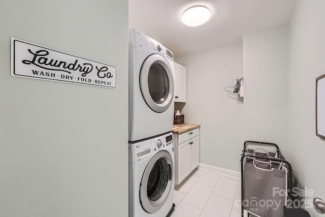 clothes washing area with cabinet space, light tile patterned flooring, baseboards, and stacked washing maching and dryer