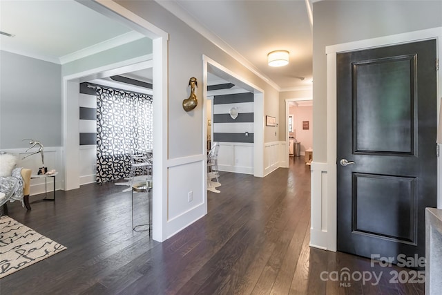 corridor featuring crown molding, a wainscoted wall, a decorative wall, and wood finished floors