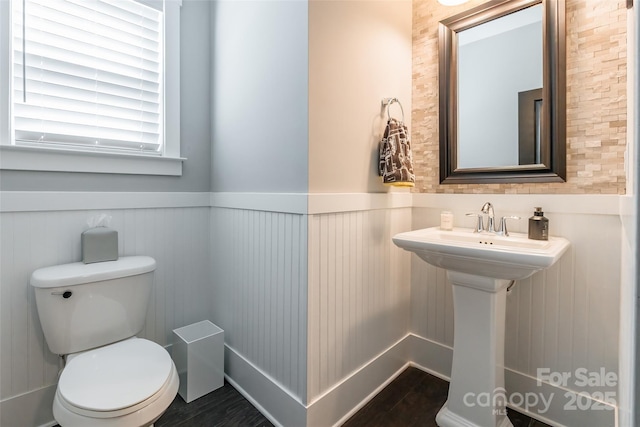bathroom with wood finished floors, toilet, a wainscoted wall, and a sink
