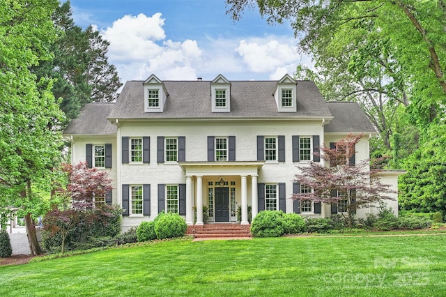 colonial home featuring roof with shingles and a front lawn