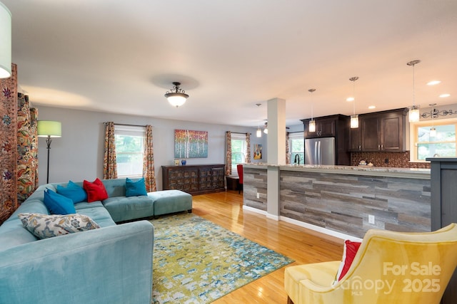 living room with healthy amount of natural light, light wood-style floors, baseboards, and recessed lighting