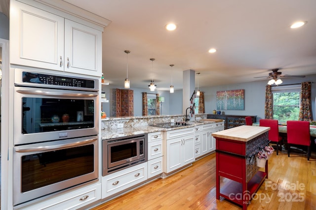 kitchen with appliances with stainless steel finishes, butcher block countertops, a peninsula, light wood-style floors, and recessed lighting