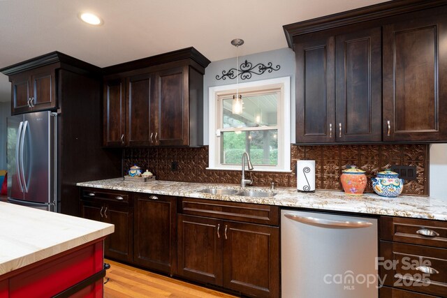 kitchen featuring stainless steel appliances, a sink, tasteful backsplash, dark brown cabinetry, and decorative light fixtures