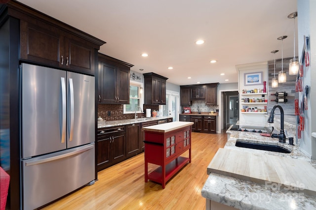 kitchen with freestanding refrigerator, open shelves, a sink, dark brown cabinetry, and light wood-style flooring