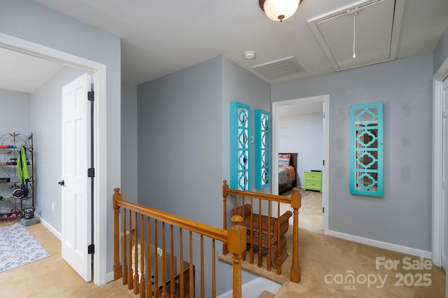 hall featuring attic access, an upstairs landing, baseboards, and carpet flooring