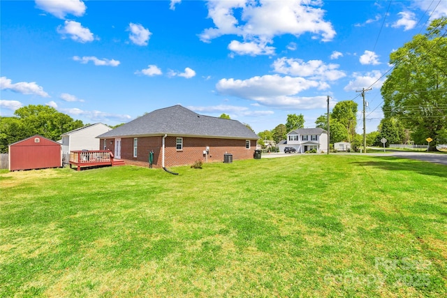 back of house with a storage shed, an outbuilding, brick siding, a deck, and a yard