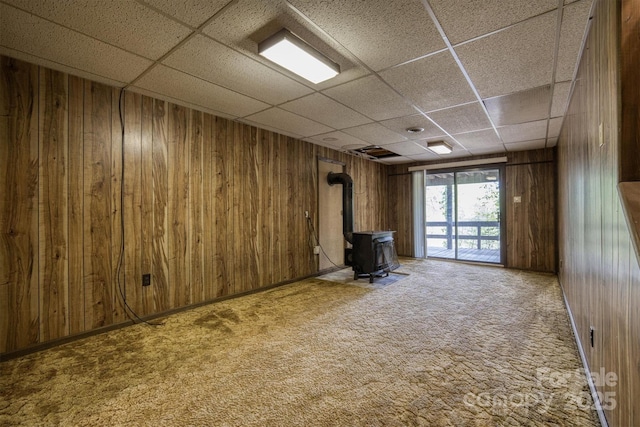 605 Hennessee St, Morganton, NC 28655 - unfurnished living room featuring a wood stove, a drop ceiling, wood walls, and carpet floors