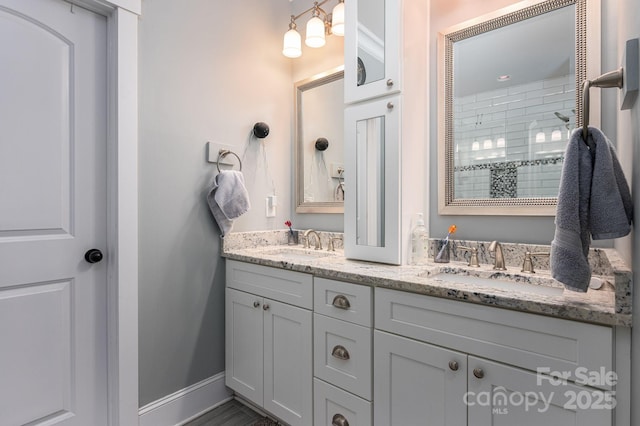 full bathroom with baseboards, a sink, a shower stall, and double vanity