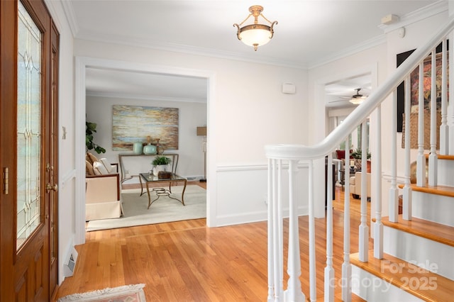 entrance foyer featuring light wood-style floors, crown molding, a ceiling fan, baseboards, and stairway