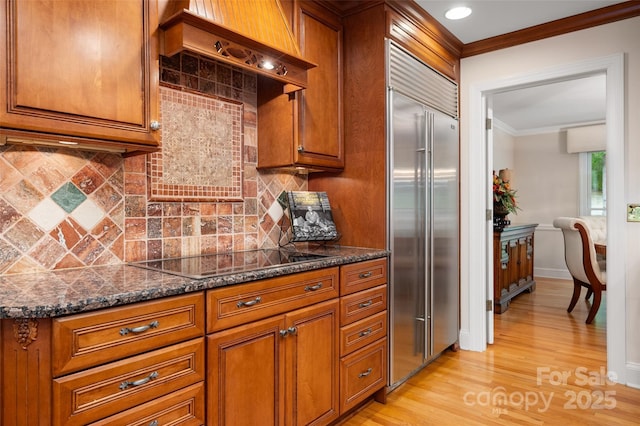 kitchen with stainless steel built in refrigerator, black electric stovetop, ornamental molding, brown cabinets, and light wood-style floors