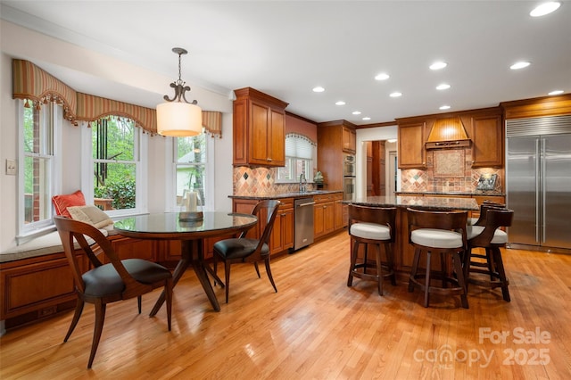 kitchen featuring appliances with stainless steel finishes, a sink, light wood-type flooring, a kitchen island, and tasteful backsplash