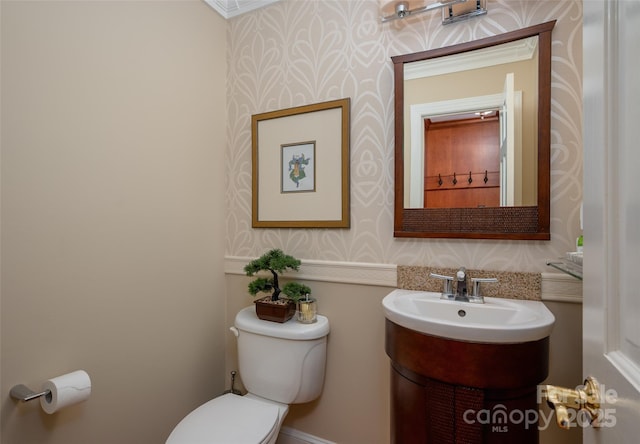 half bathroom featuring wallpapered walls, toilet, and vanity