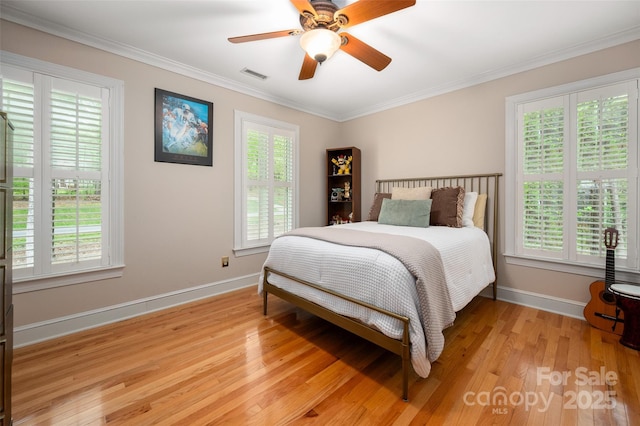 bedroom with multiple windows, light wood-style flooring, baseboards, and crown molding