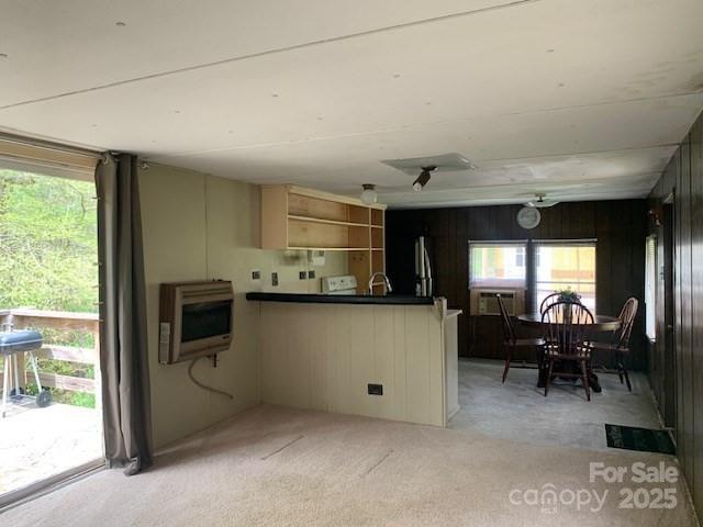 kitchen featuring heating unit, open shelves, a sink, a peninsula, and light colored carpet
