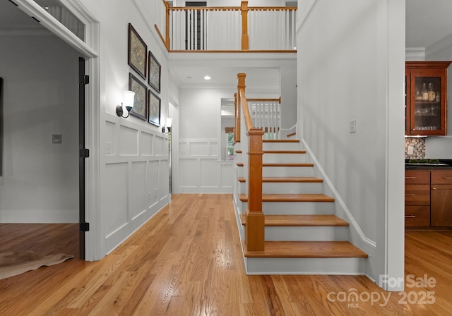 staircase featuring crown molding, a wainscoted wall, wood finished floors, and a decorative wall