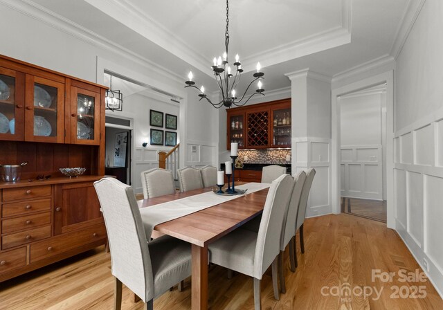 dining room with ornamental molding, light wood-style flooring, a dry bar, and a decorative wall