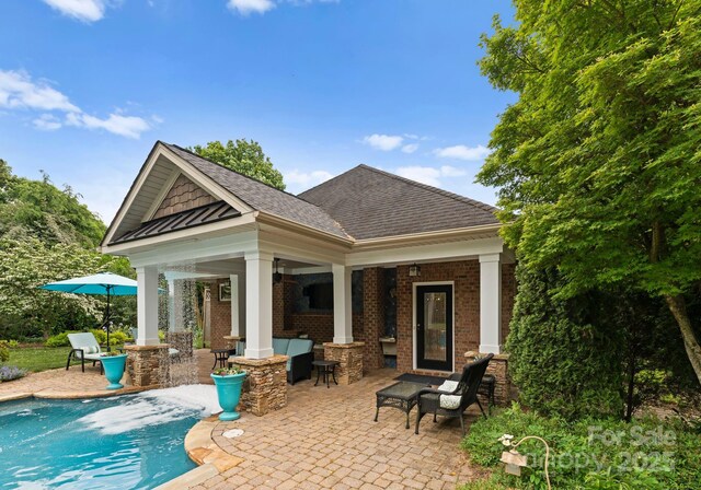 back of property featuring brick siding, a shingled roof, a patio area, and an outdoor pool