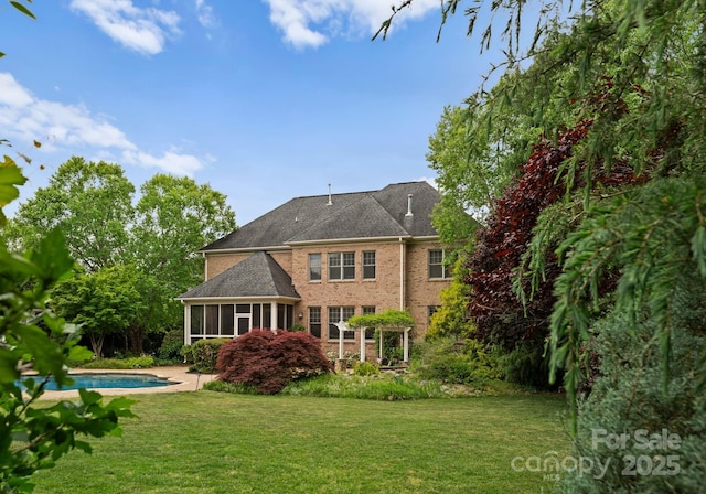 rear view of house featuring a yard, brick siding, an outdoor pool, and a sunroom
