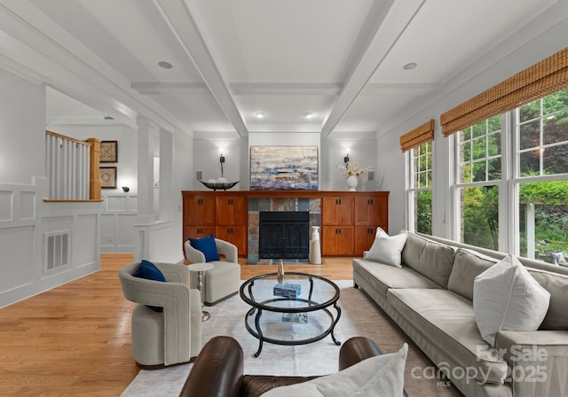 living area with a decorative wall, light wood-style flooring, a tile fireplace, beamed ceiling, and visible vents