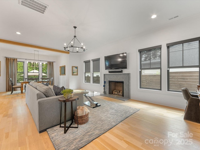 living room with a fireplace, an inviting chandelier, visible vents, and light wood-style flooring