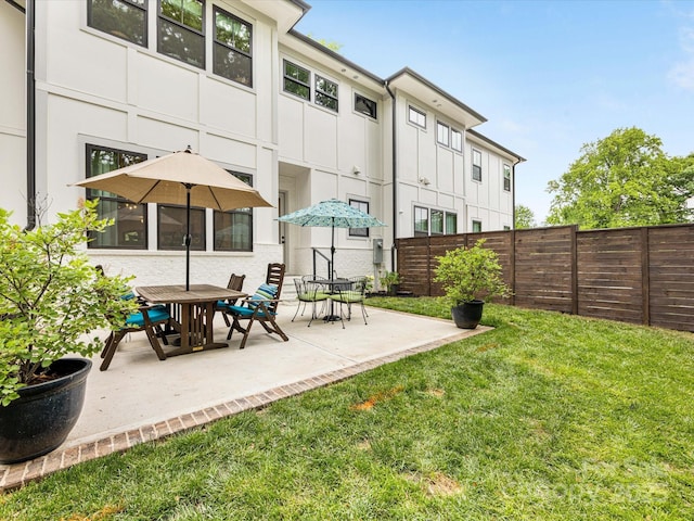 rear view of house with fence, a lawn, and a patio area