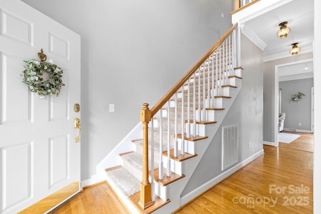 entrance foyer featuring visible vents, ornamental molding, stairs, and wood finished floors