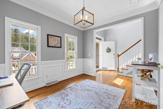 office area featuring an inviting chandelier, crown molding, a wainscoted wall, visible vents, and wood finished floors