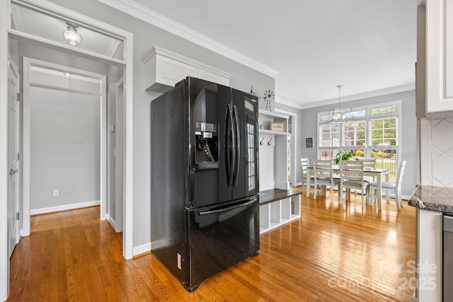 kitchen with ornamental molding, light wood-style floors, black fridge, and white cabinets