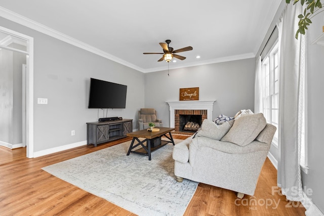living room with crown molding, light wood-style flooring, baseboards, a fireplace, and a ceiling fan
