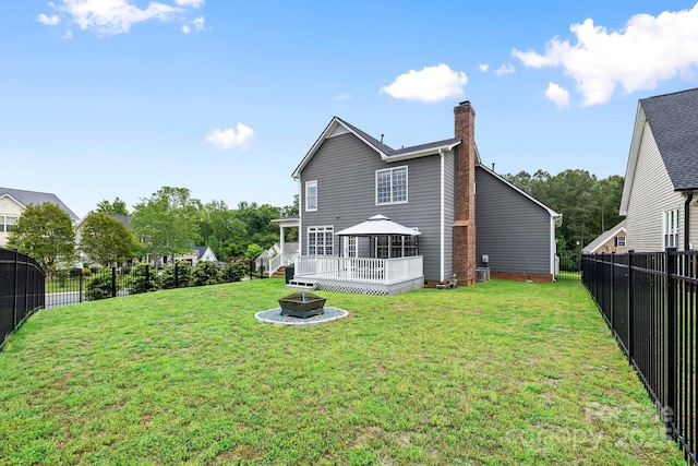 rear view of house featuring a fenced backyard, a lawn, a chimney, a gazebo, and a fire pit