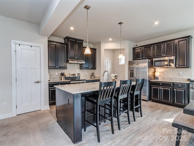 kitchen with backsplash, under cabinet range hood, stainless steel appliances, and a kitchen island with sink