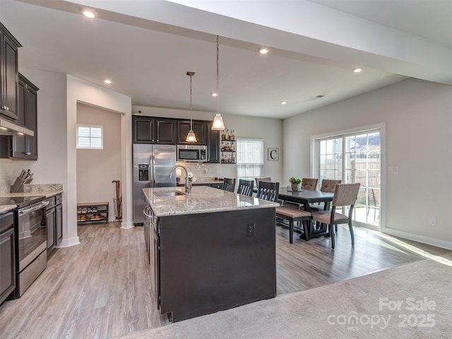 kitchen with a sink, a kitchen island with sink, a wealth of natural light, appliances with stainless steel finishes, and light stone countertops