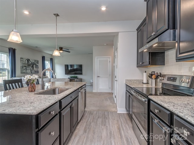 kitchen featuring a sink, light wood-type flooring, open floor plan, under cabinet range hood, and appliances with stainless steel finishes