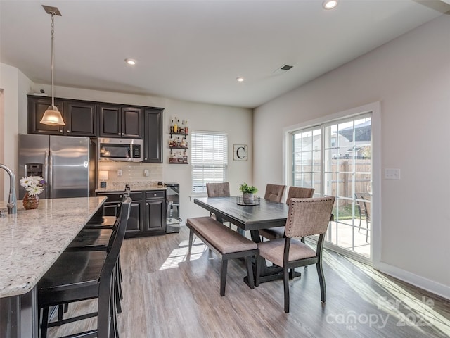 dining space with indoor bar, light wood-type flooring, baseboards, recessed lighting, and visible vents