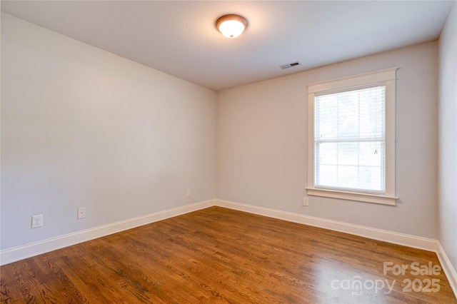 unfurnished room featuring visible vents, baseboards, and dark wood-style flooring