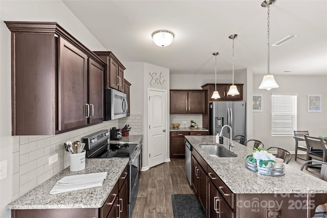 kitchen with appliances with stainless steel finishes, a sink, dark wood finished floors, a center island with sink, and dark brown cabinetry